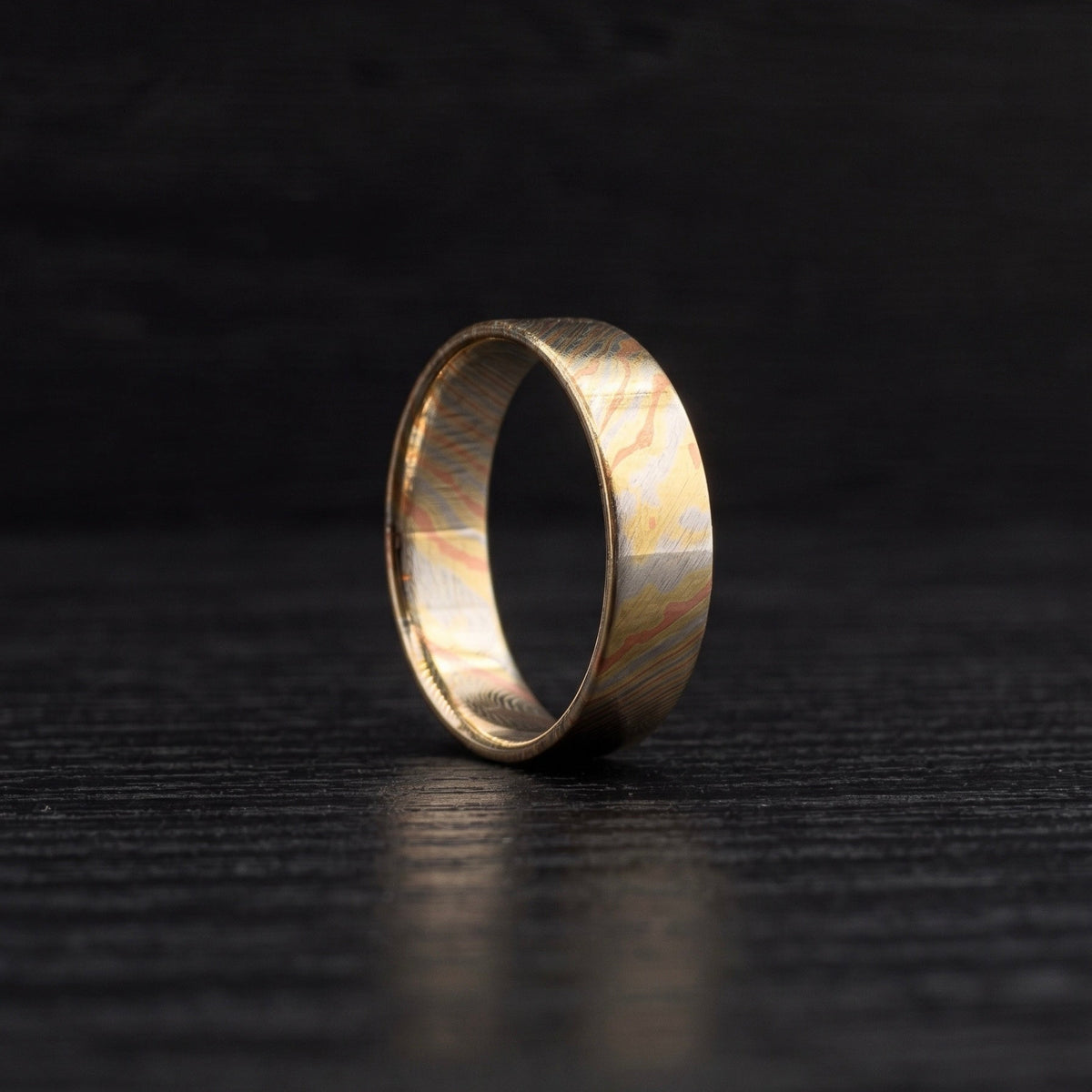 A single gold-toned ring with a textured, patterned inlay, standing upright on a dark, textured wooden surface.